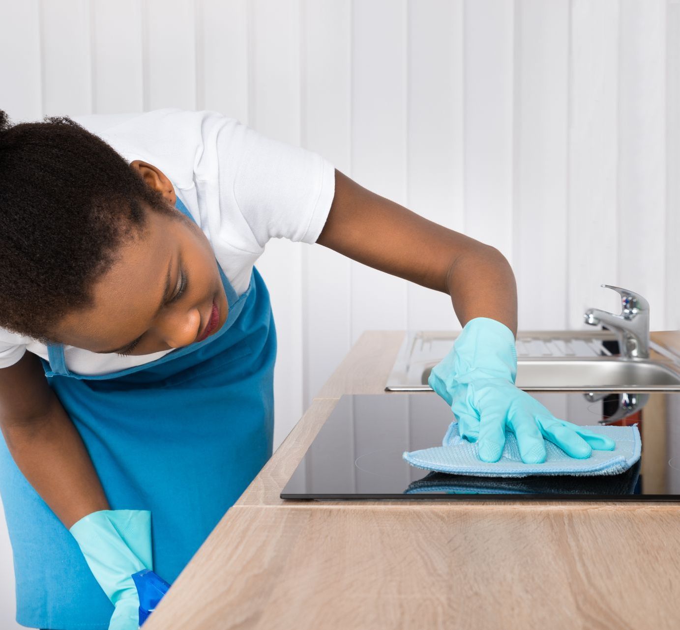 A woman wearing blue gloves is cleaning a sink