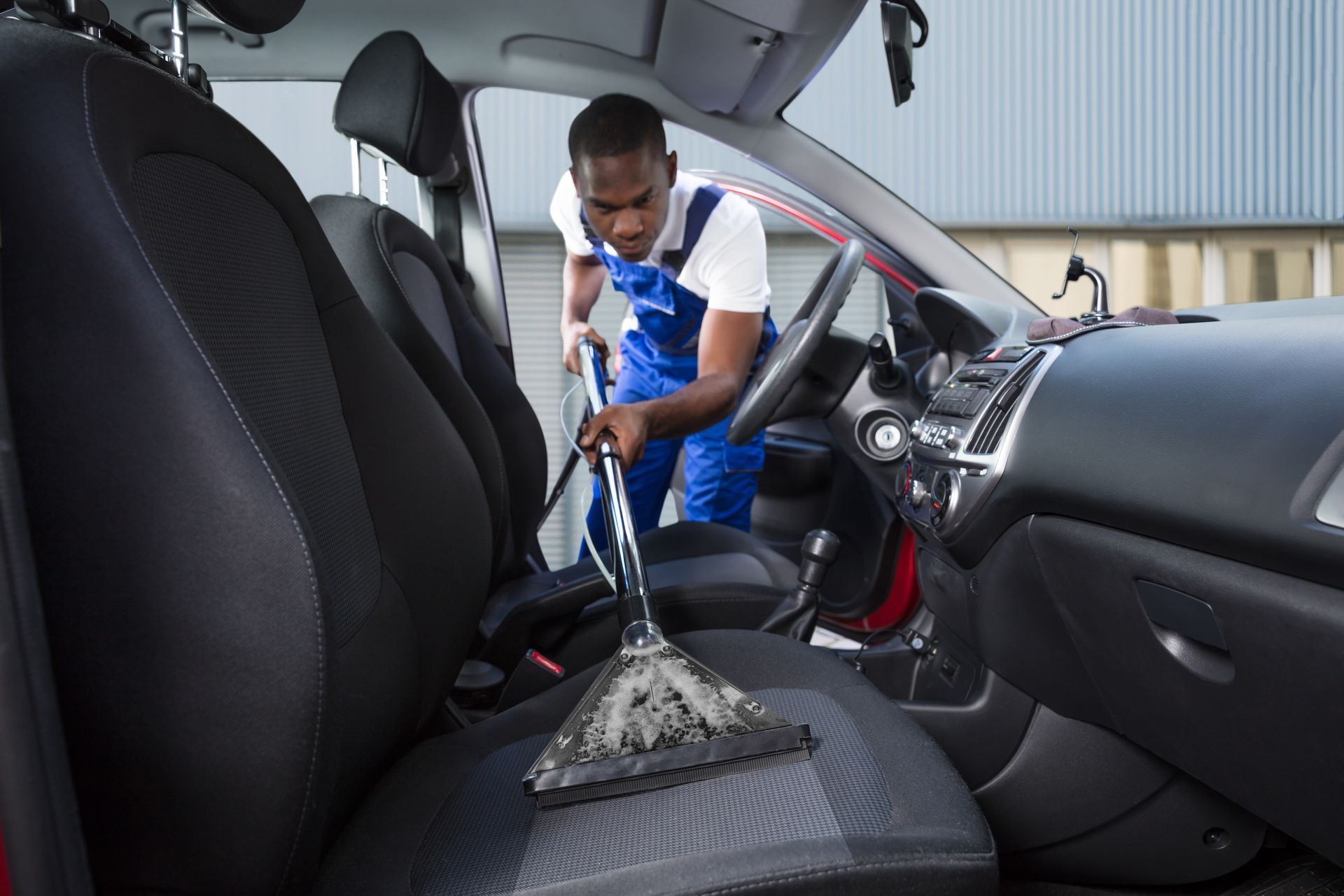 A man is cleaning the seats of a car with a vacuum cleaner.