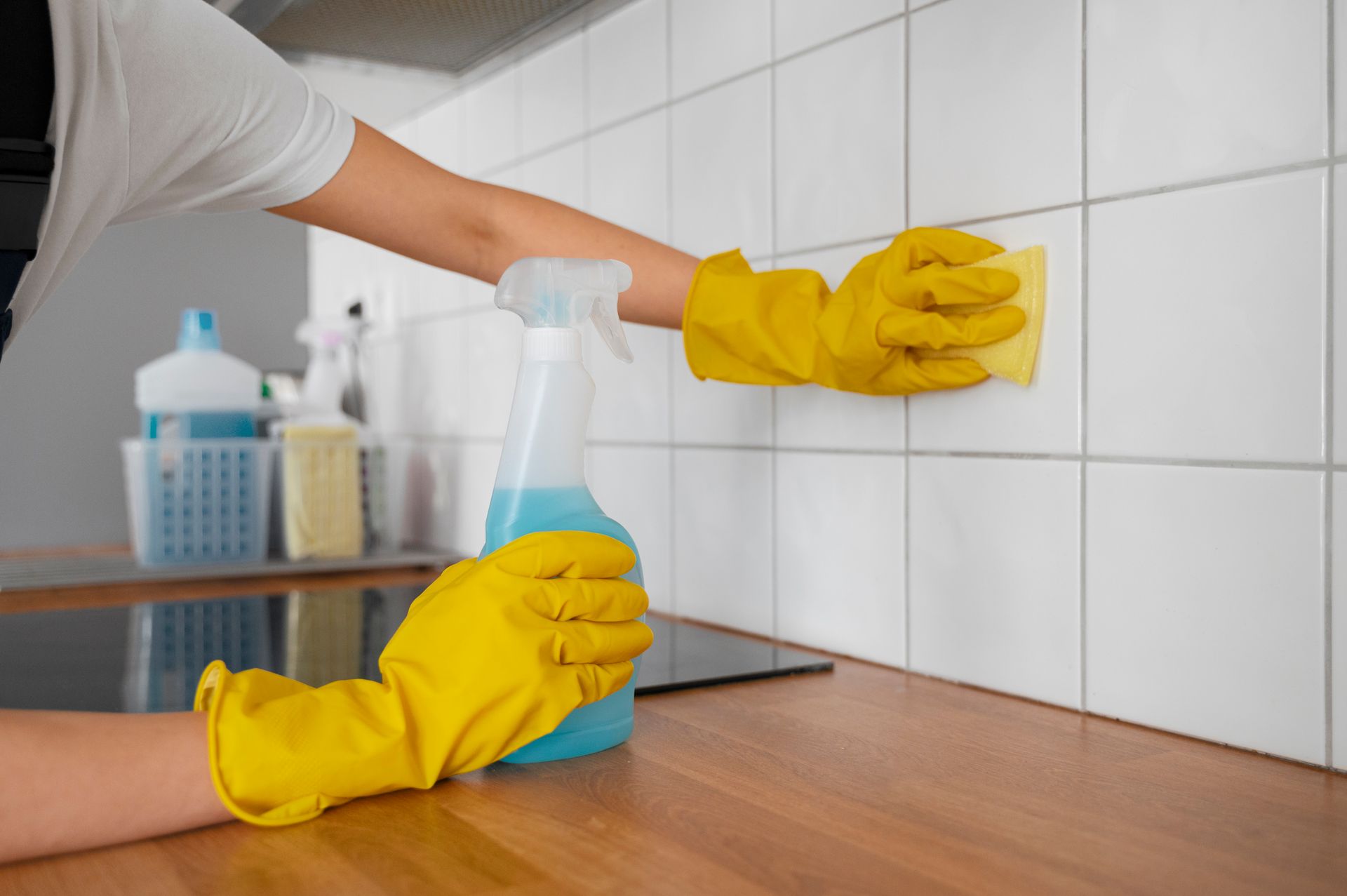 A person wearing yellow gloves is cleaning a tile wall in a kitchen.