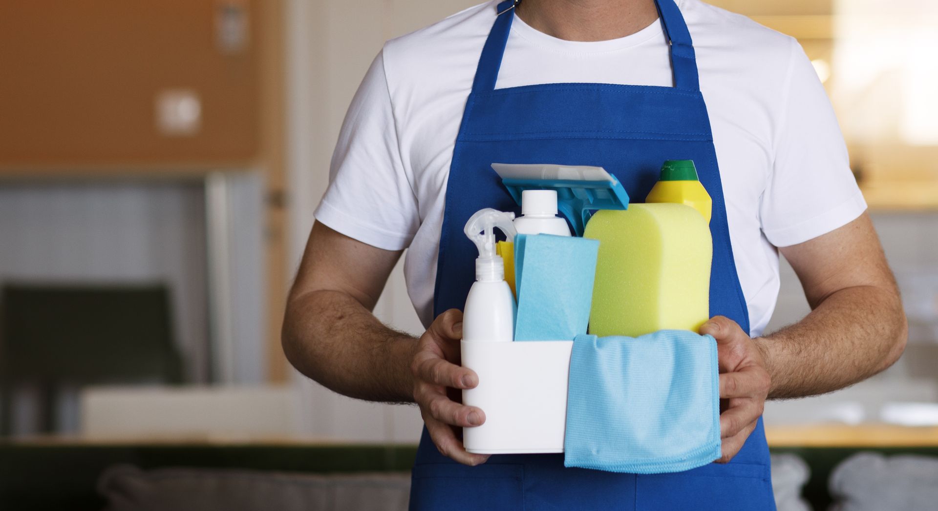 A man in an apron is holding cleaning supplies in his hands.