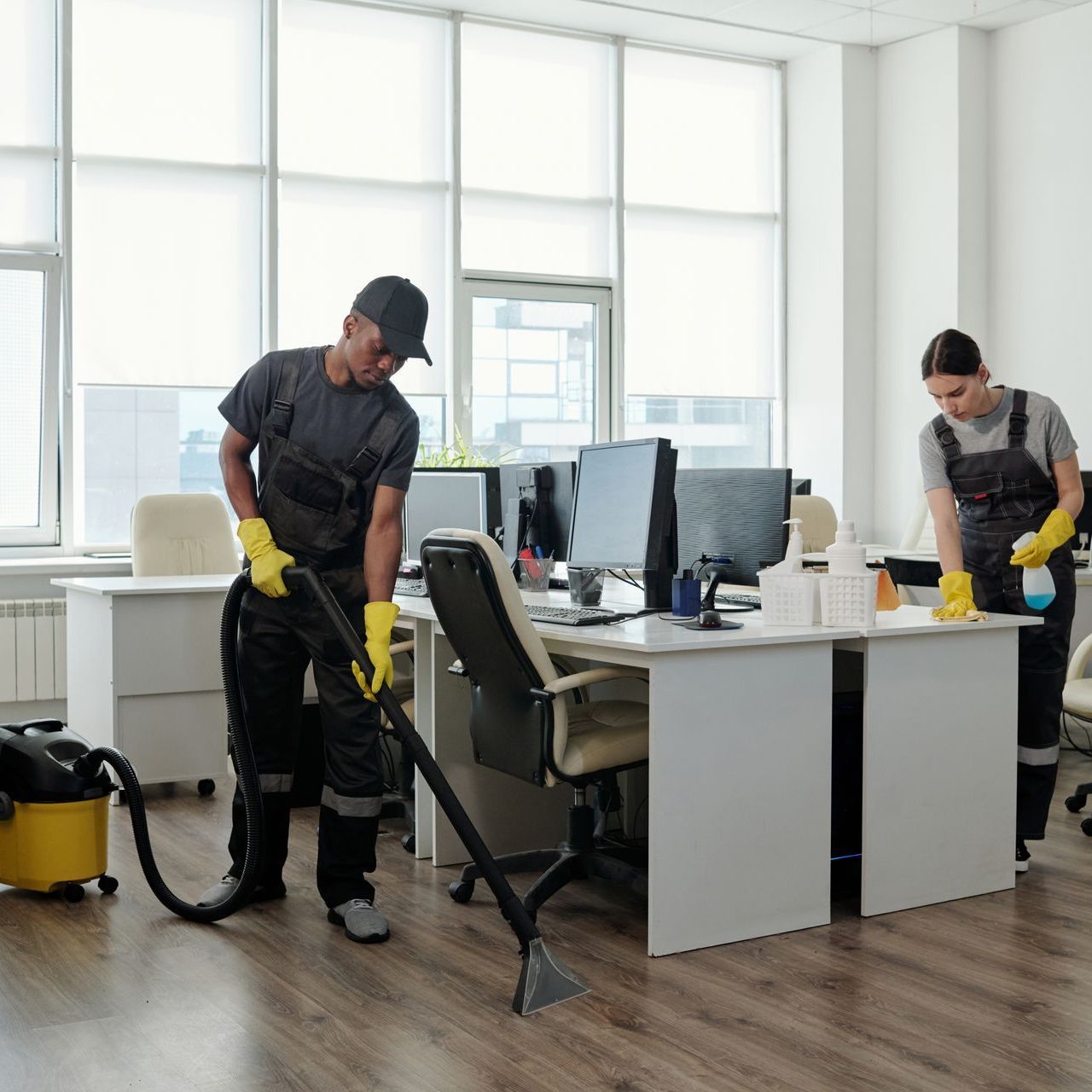 A man and a woman are cleaning an office with a vacuum cleaner.