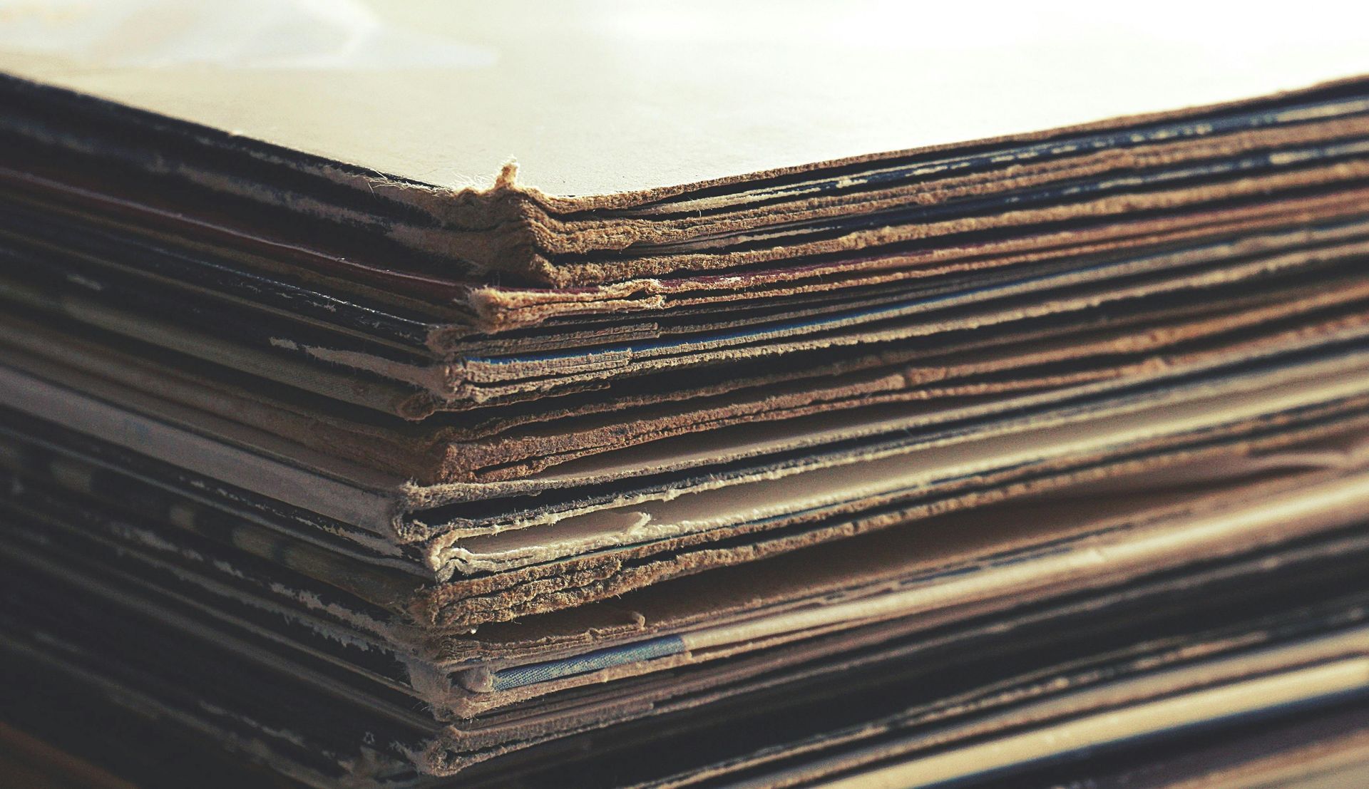 Stack of old, worn vinyl record albums, showing edges and paper sleeves.