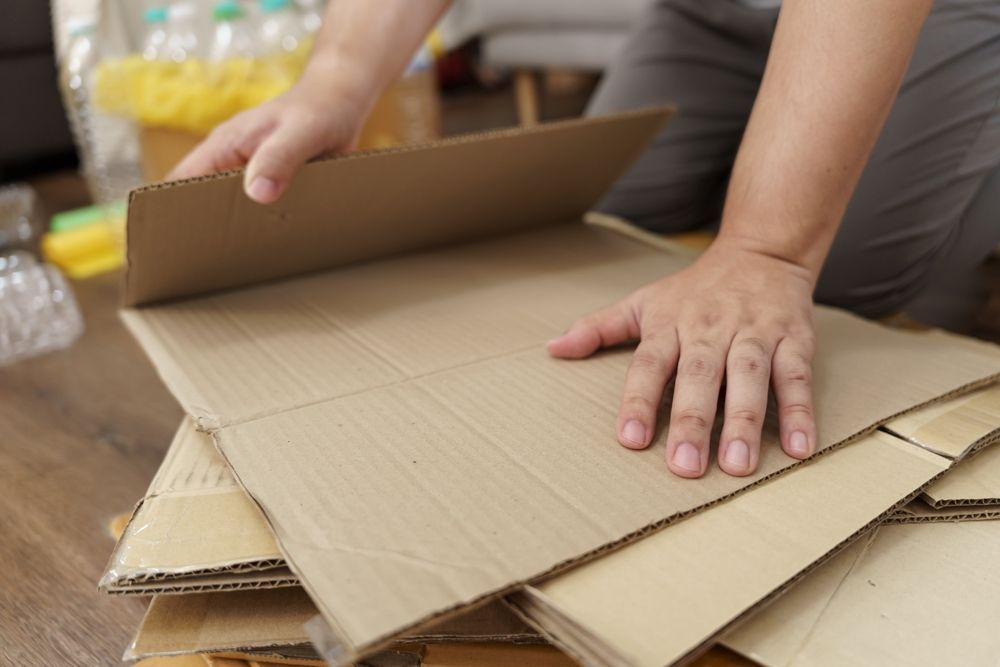 Person stacking cardboard sheets on a wooden floor, indoor setting.