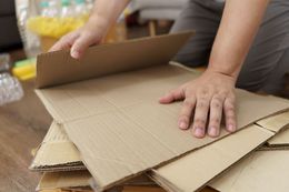 Person stacking cardboard sheets on a wooden floor, indoor setting.