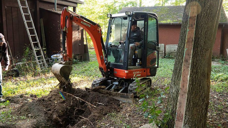 A man is driving a small excavator in a yard.