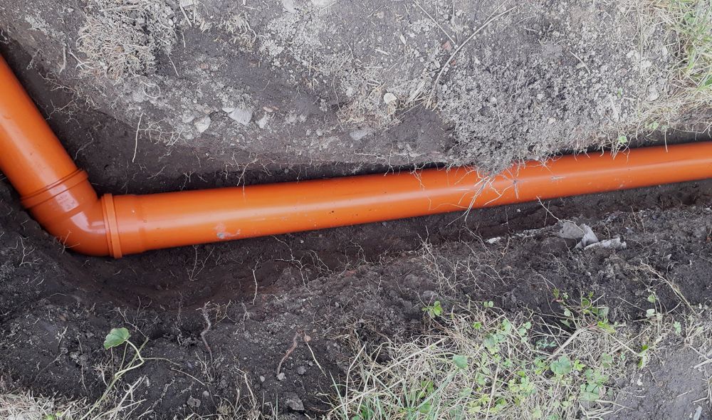 An orange pipe is laying in the dirt on the ground.