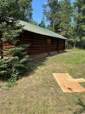 A log cabin with a green roof is sitting in the middle of a grassy field.