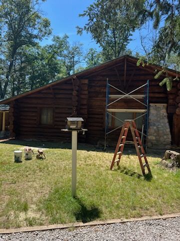 A woman is cleaning a log cabin with a high pressure washer.