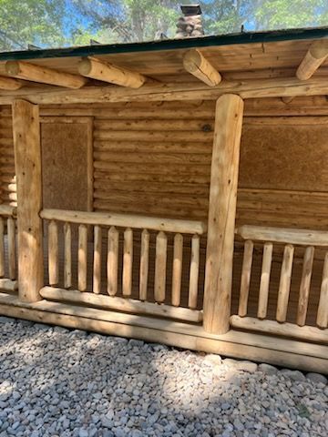 A log cabin with a porch and railing is sitting on top of a pile of gravel.