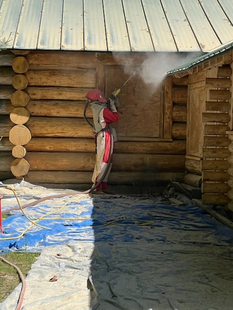 A man is sandblasting a log cabin with a hose