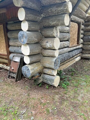 A man in a yellow raincoat is painting a log cabin.