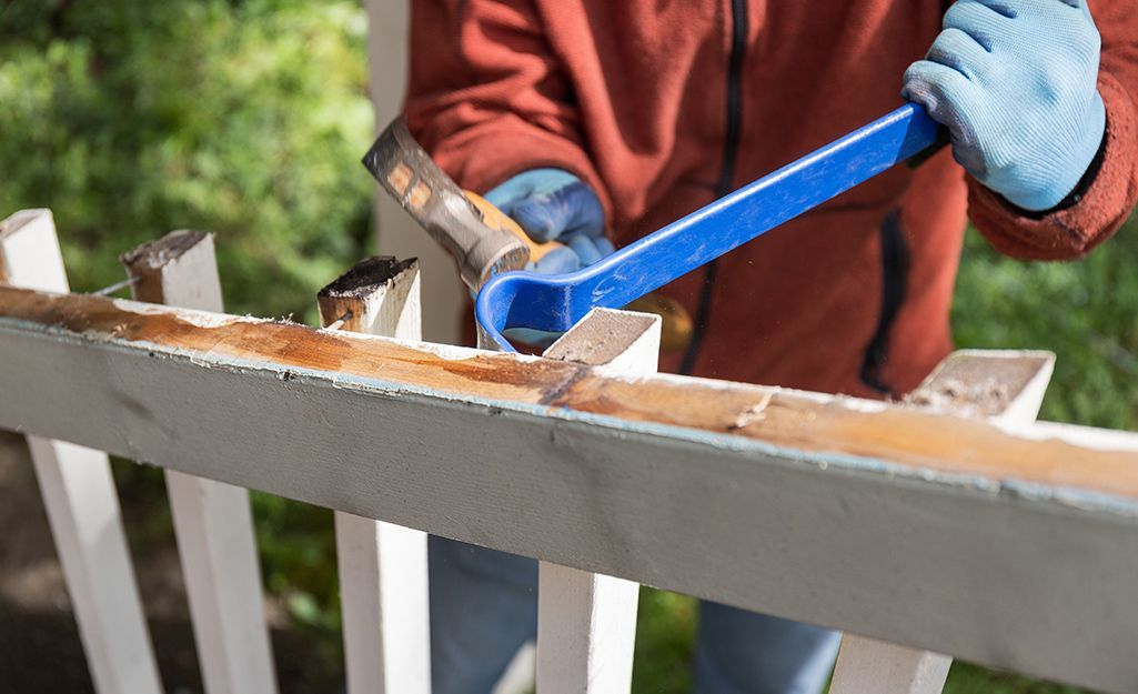 A man is using a wrench to remove a piece of wood from a fence.