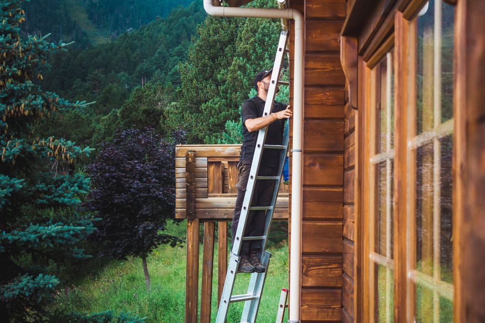 A man is standing on a ladder on the side of a wooden house.