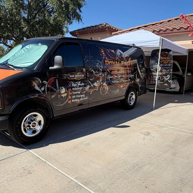 Black decorated van and canopy tent parked in a sunny driveway outside a house