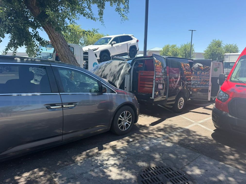 Dark minivan towing a trailer loaded with a white SUV in a sunny parking lot