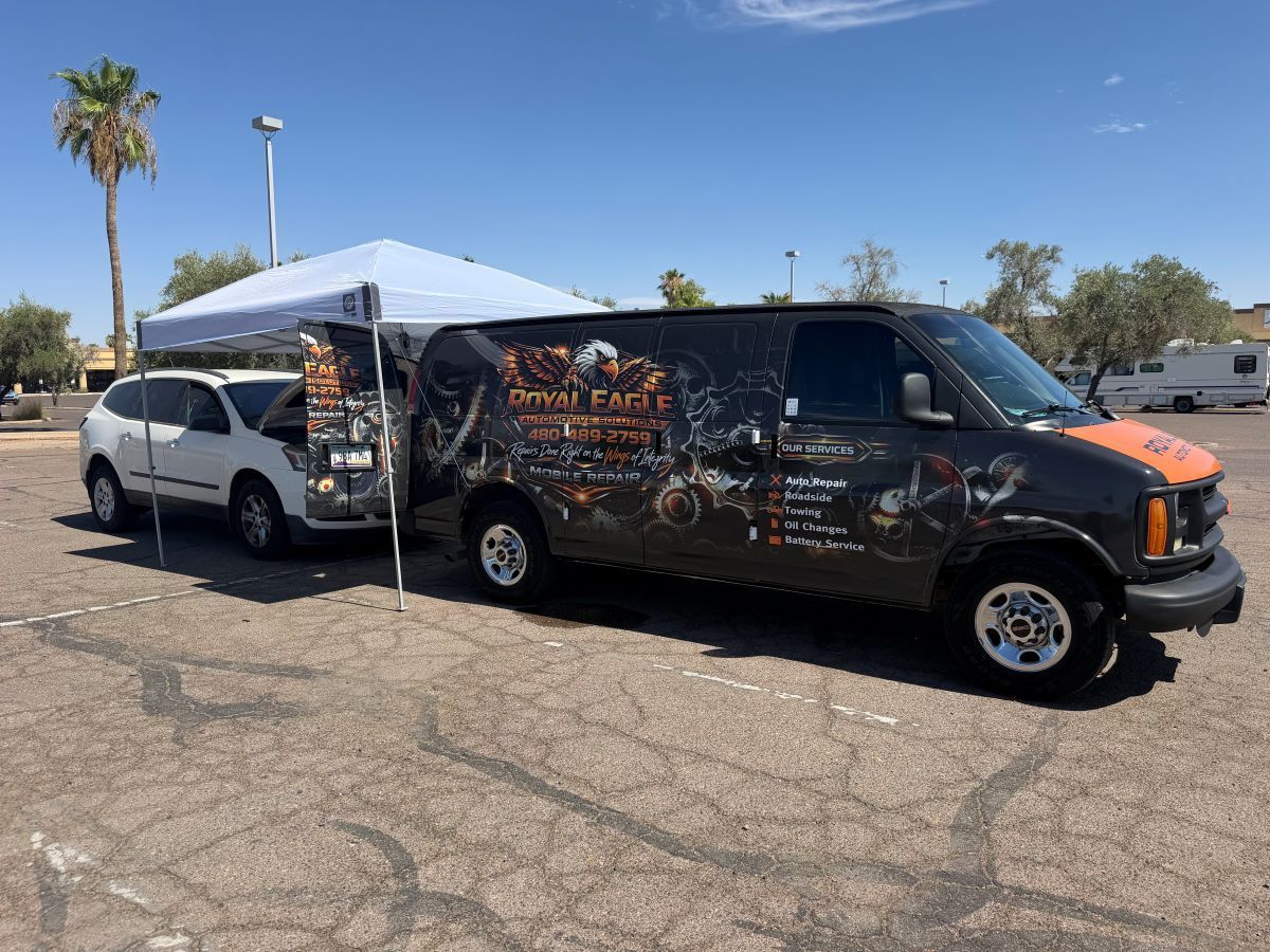 Black van with colorful graphics parked beside a white SUV under a canopy in a sunny lot