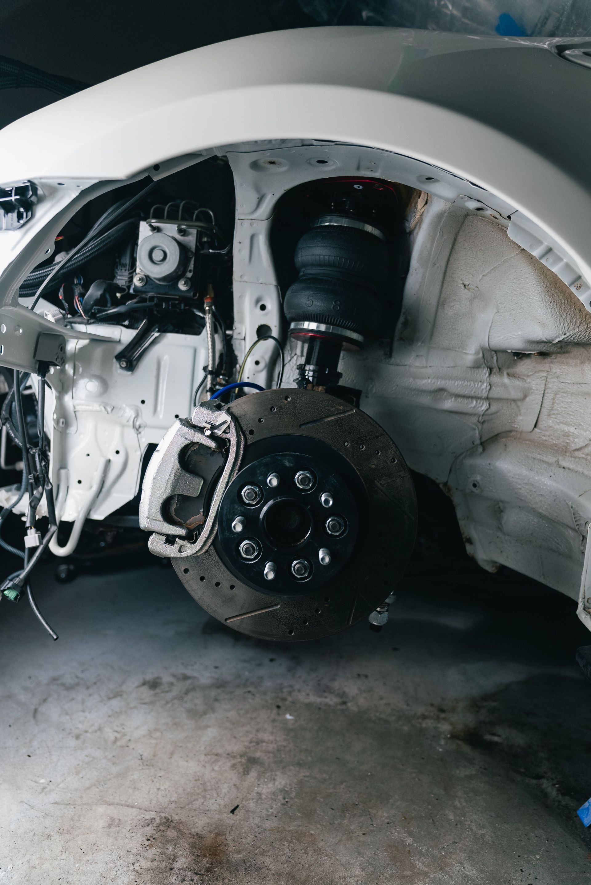 Car wheel well exposed during repair, with suspension and brake assembly visible under a white car.