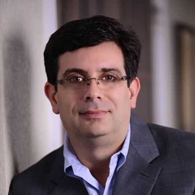 A man in a suit and glasses is leaning against a wall.