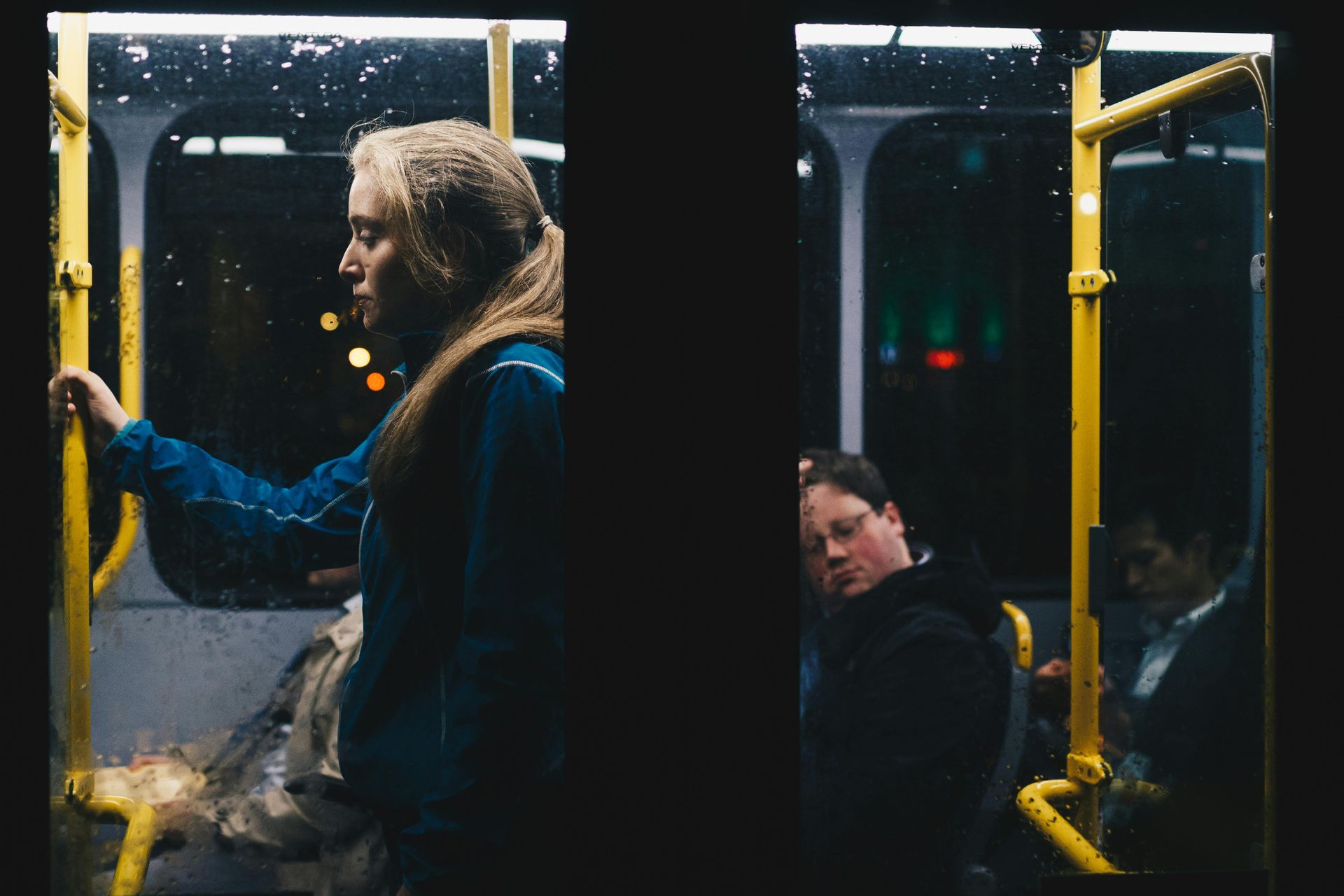 A woman is holding onto a yellow railing on a bus.