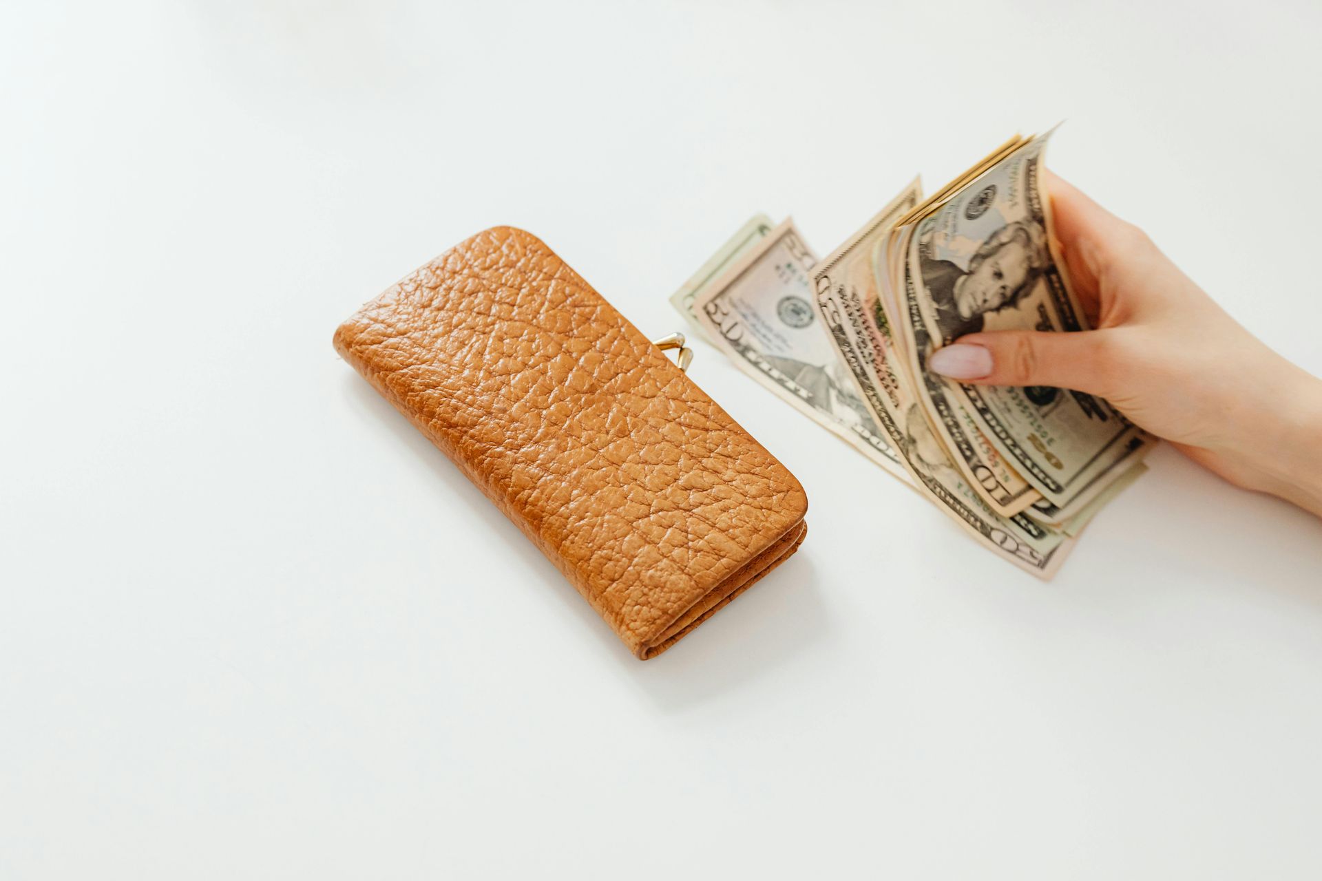 A person is holding a bunch of money next to a wallet.