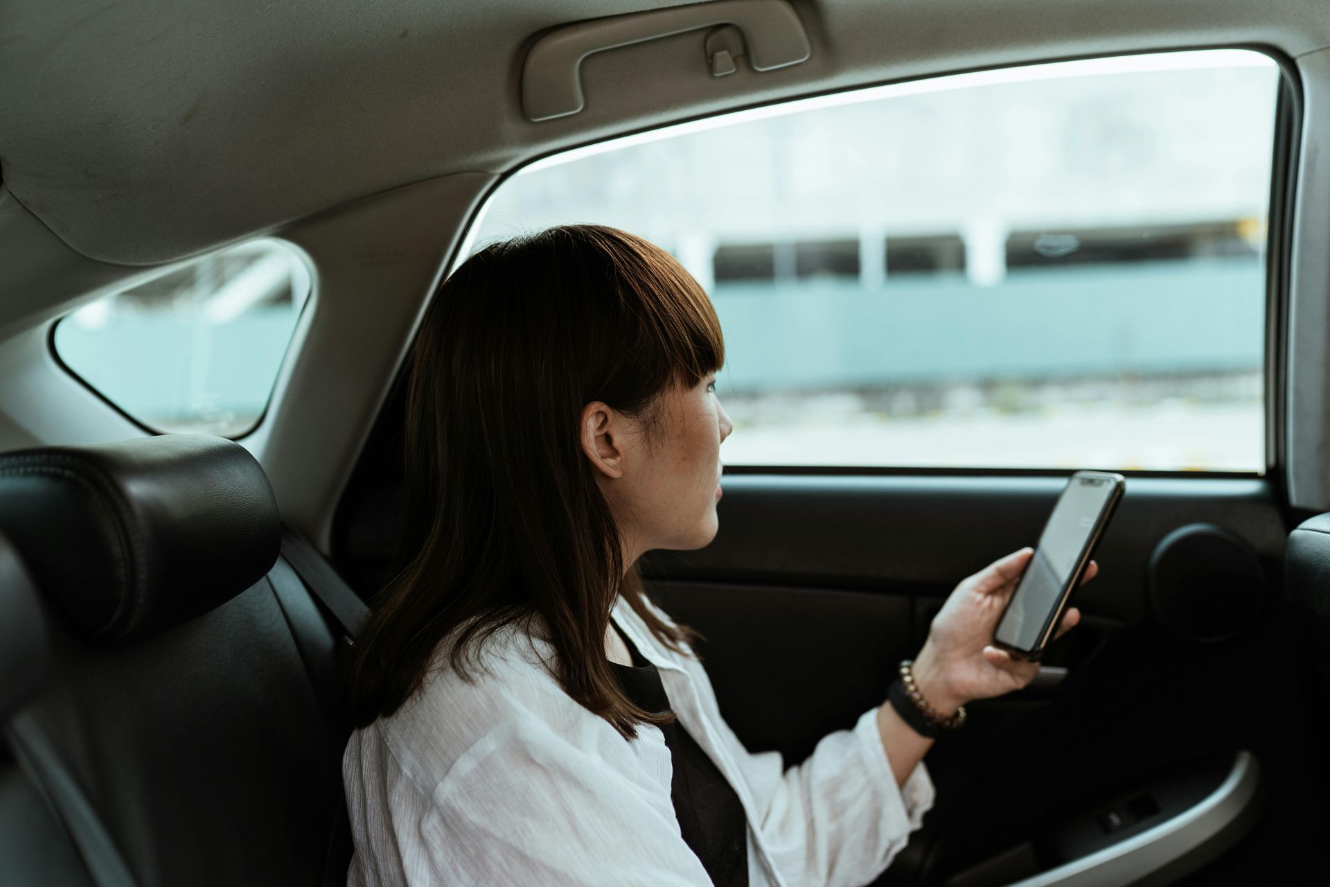 A woman is sitting in the back seat of a car looking at her phone.