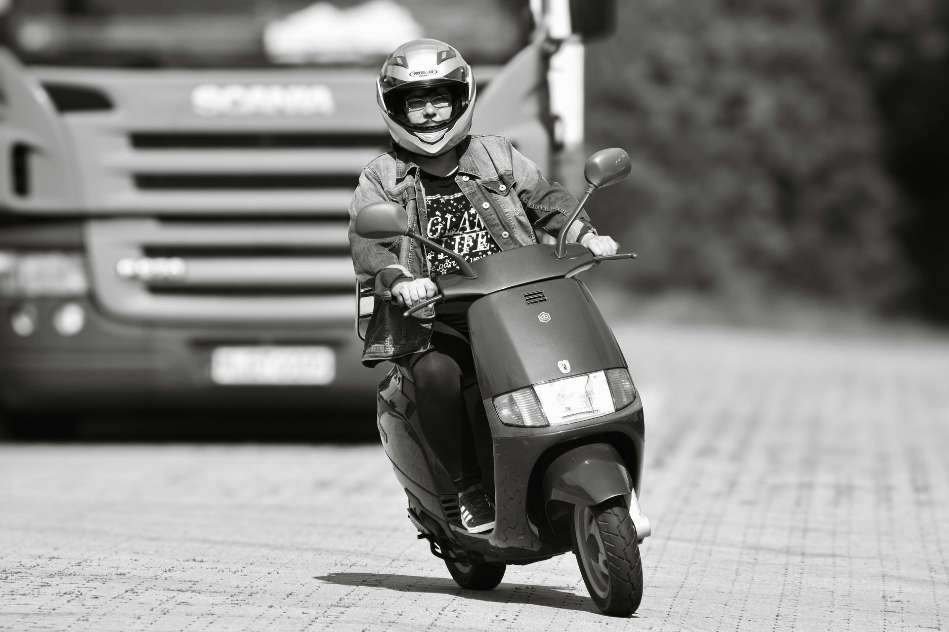 A man is riding a scooter in front of a truck.