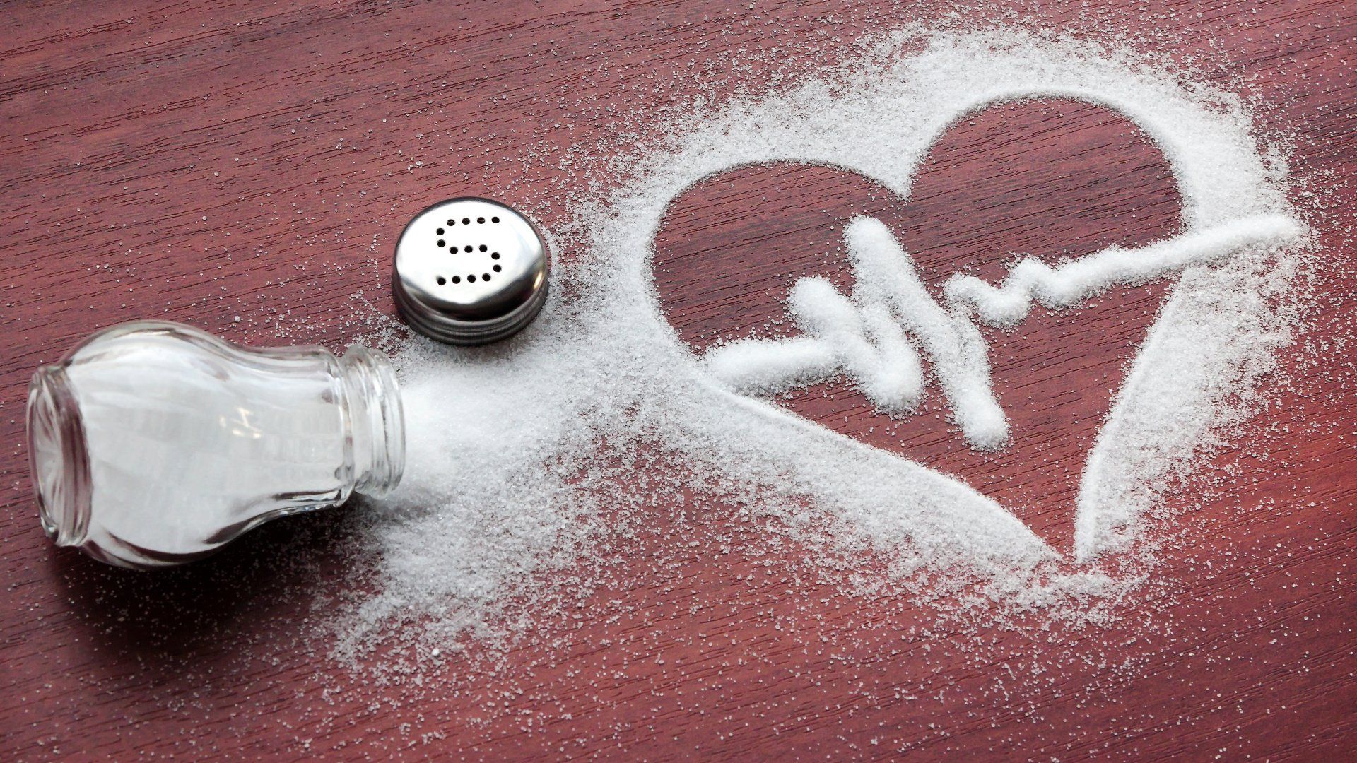 A salt shaker and a heart drawn in salt on a table.