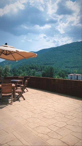 Un patio con tavoli, sedie e un ombrellone si affaccia su una montagna sotto un cielo nuvoloso.