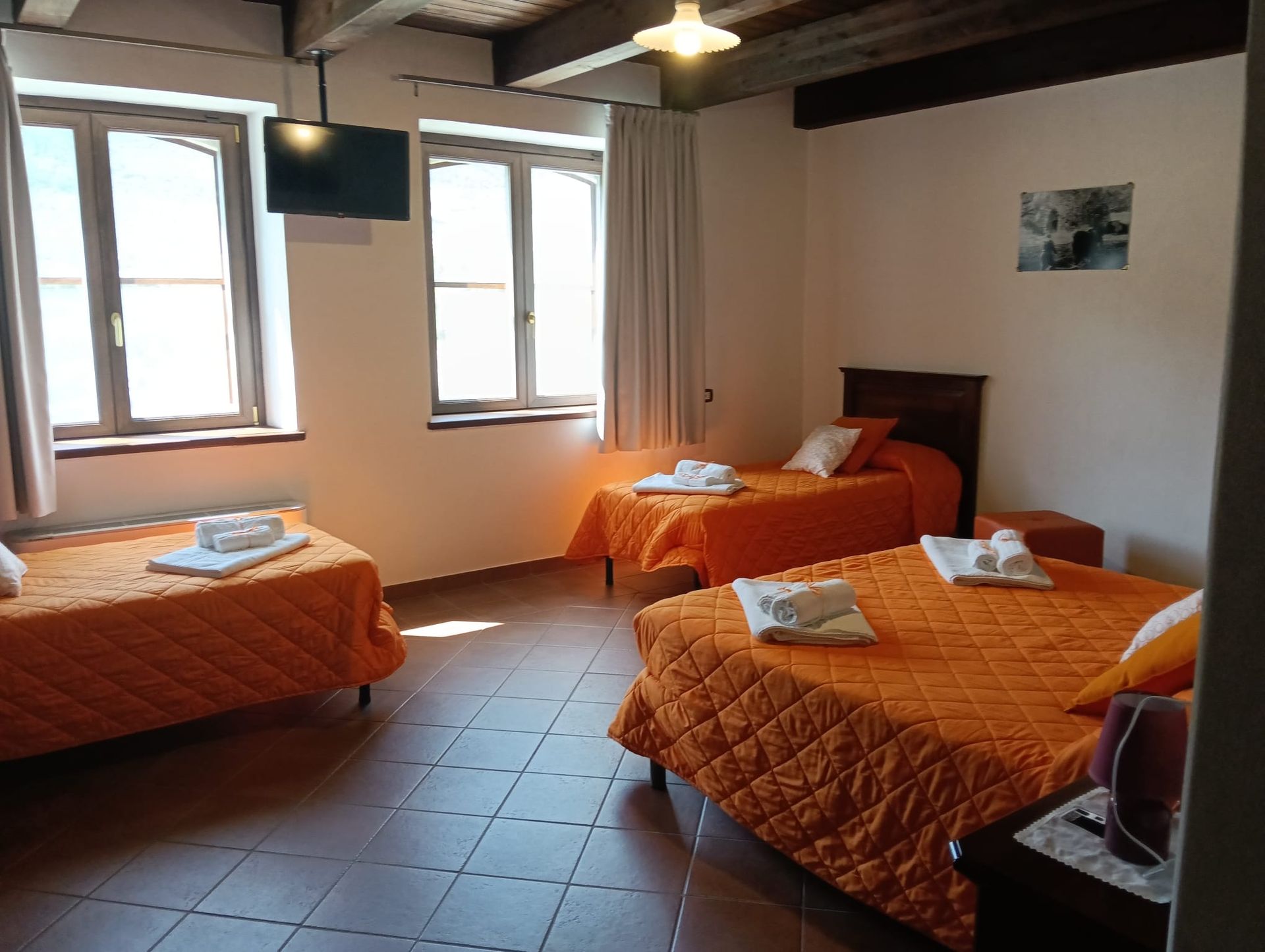 Una camera con tre letti singoli, ciascuno con un piumone arancione. Due finestre forniscono luce.