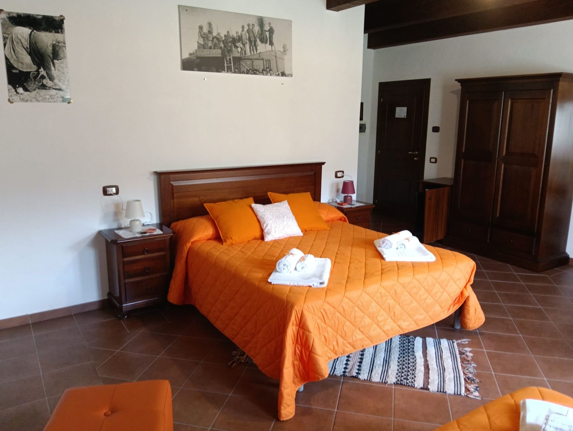 Camera da letto con copriletto arancione, comodini, armadio in legno e opere d'arte.
