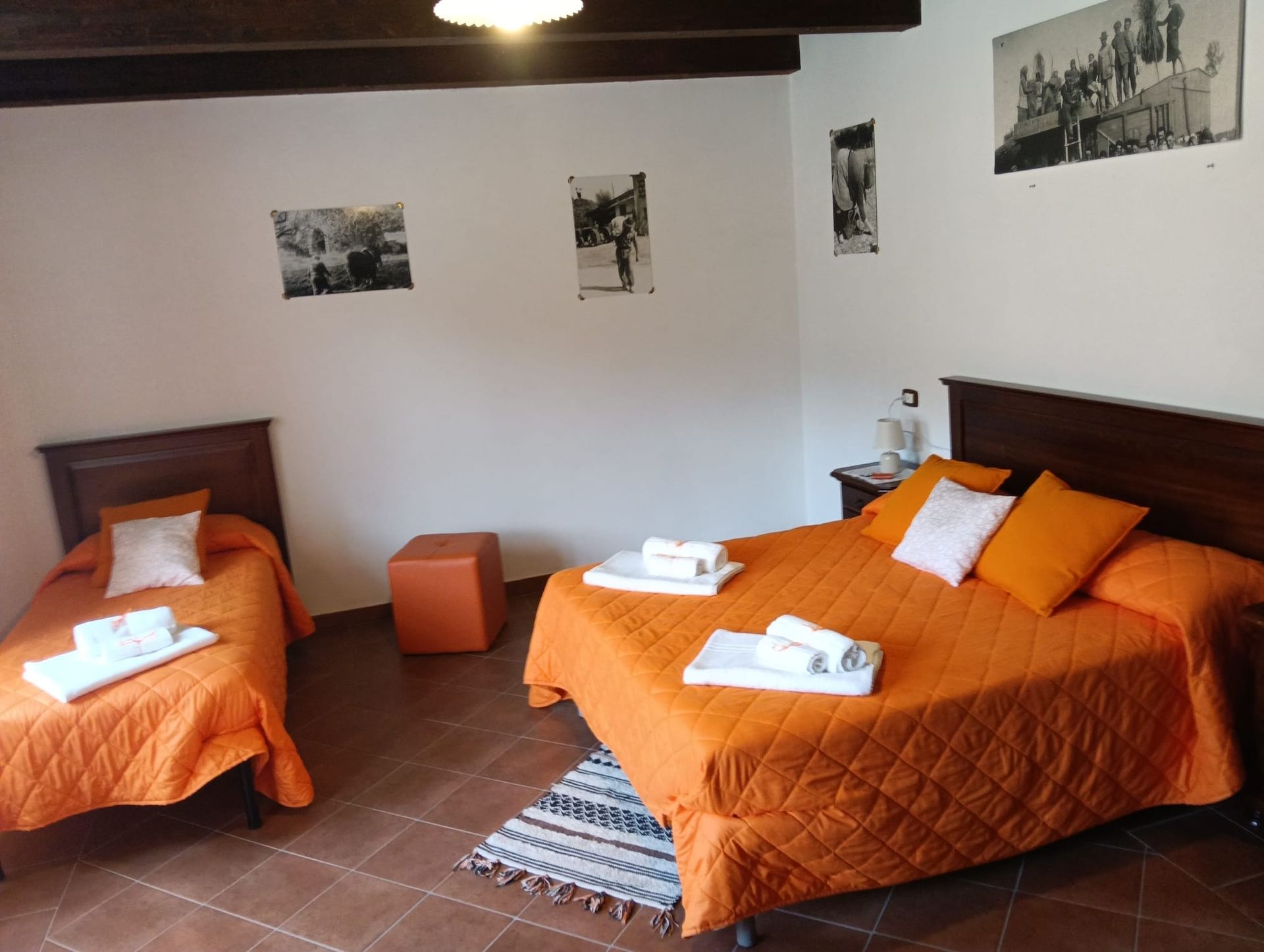 Camera da letto con due letti ricoperti di lenzuola arancioni, foto sulle pareti bianche e pavimento in piastrelle marroni.