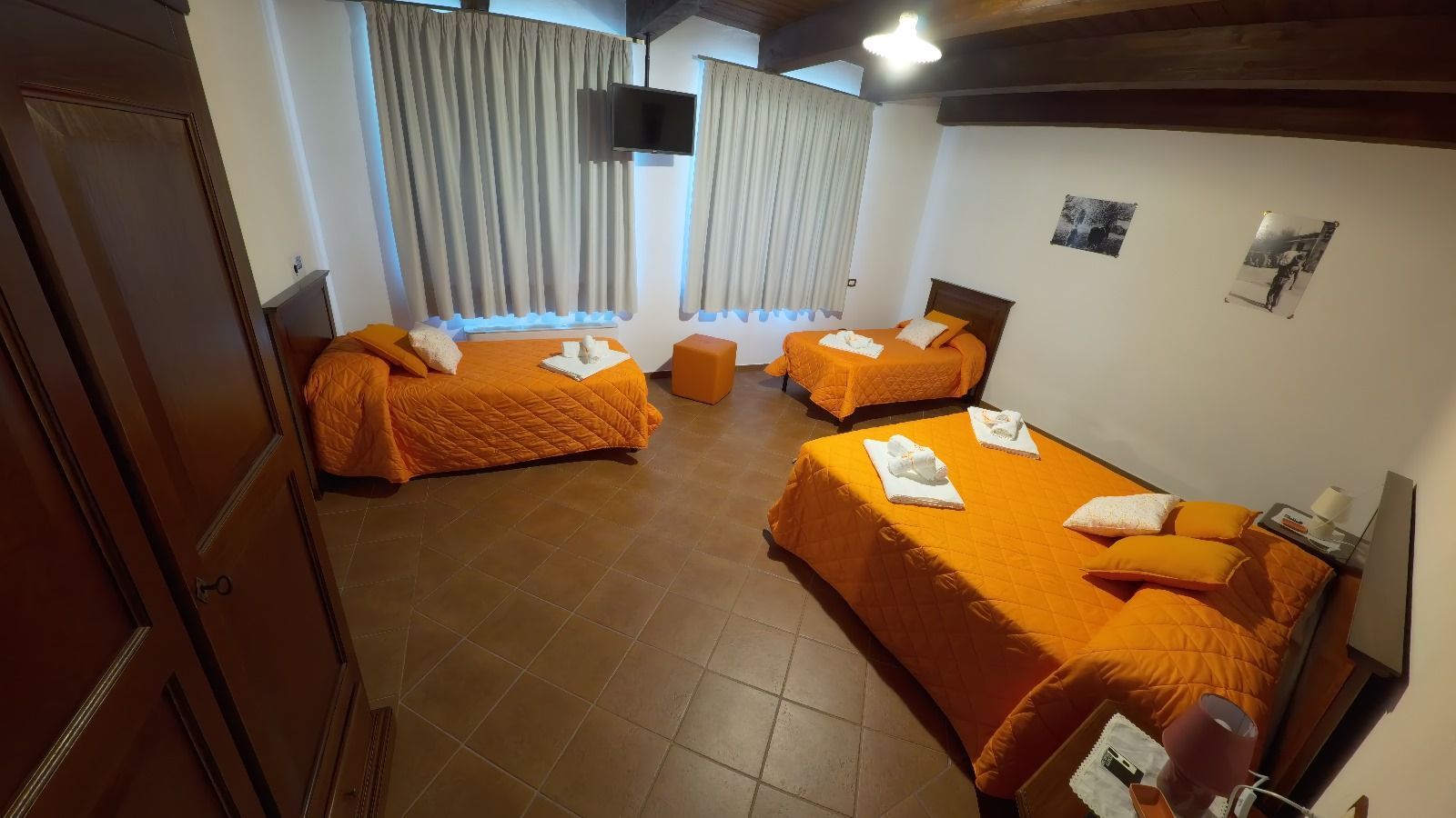 Una camera d'albergo con tre letti, lenzuola arancioni, pavimenti in piastrelle marroni e una piccola TV.