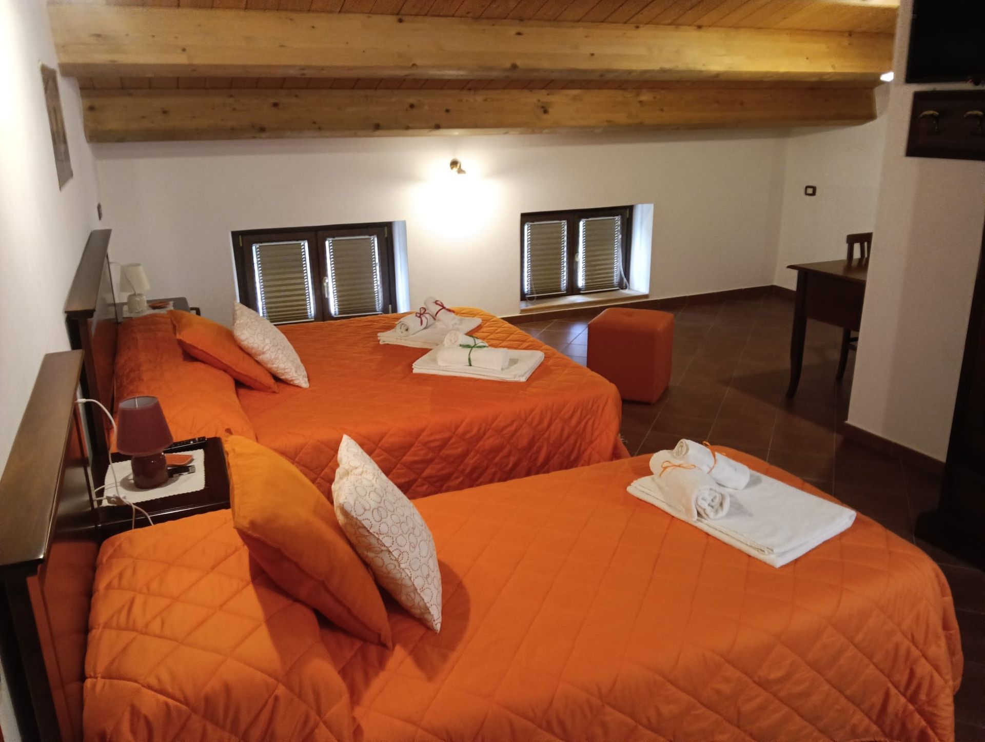 Una camera da letto con due letti arancioni, travi in legno e piccole finestre.