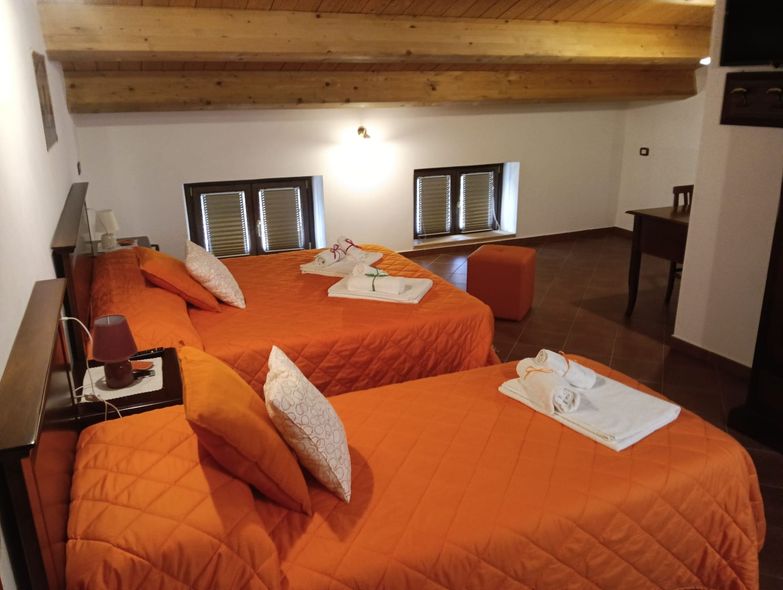 Una camera da letto con due letti arancioni, travi in legno e piccole finestre.