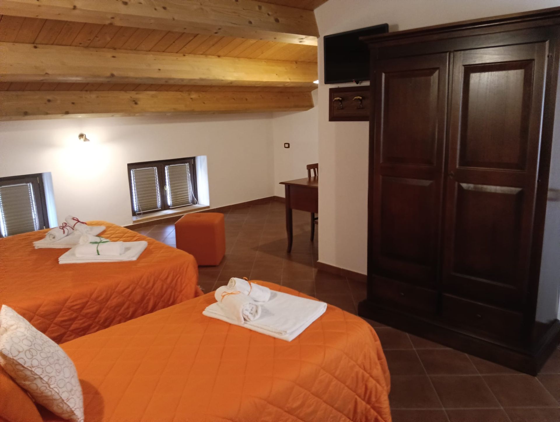 Due letti singoli con coperte arancioni in una camera da letto rustica con armadio in legno.