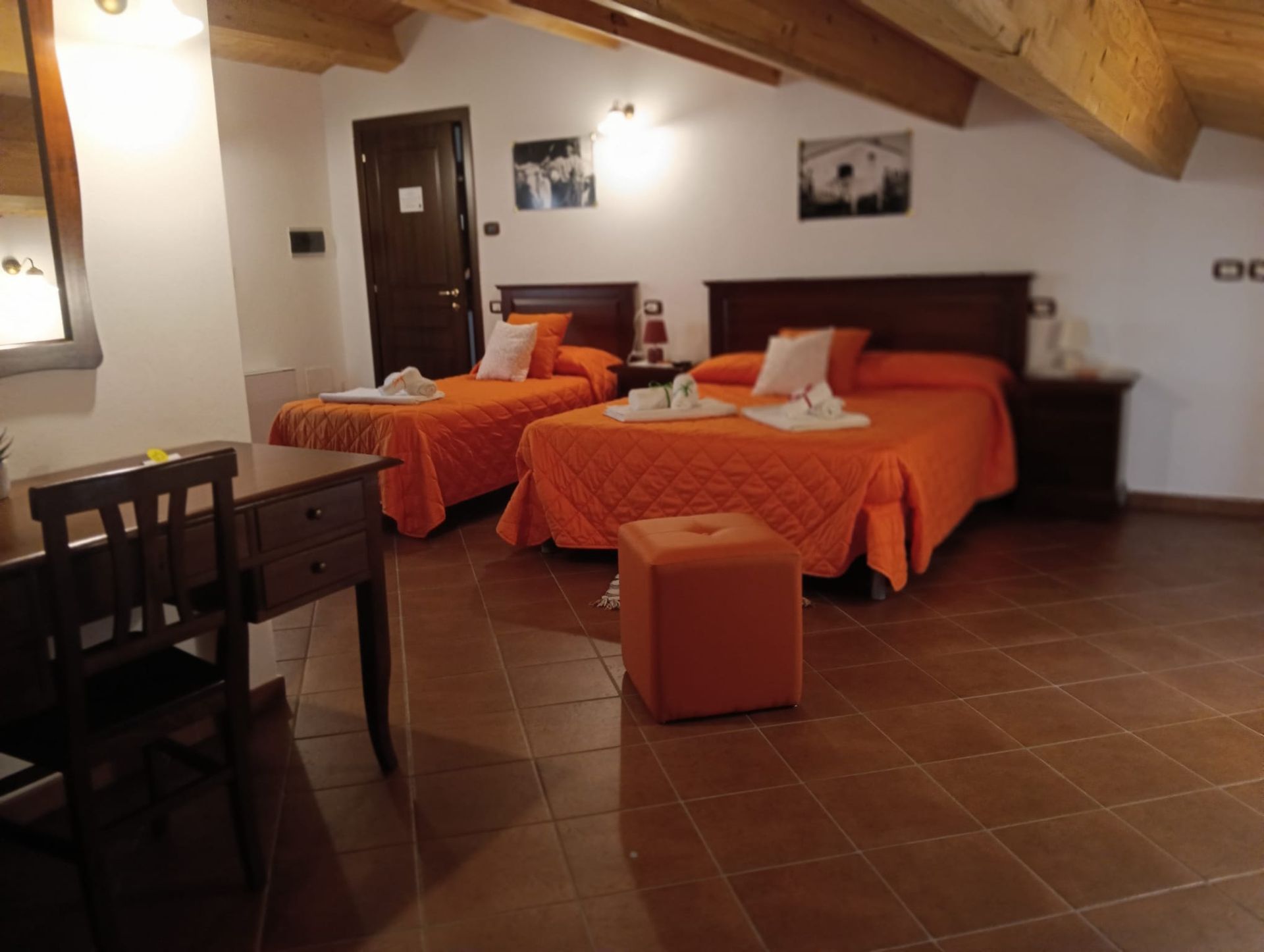 Una camera d'albergo molto luminosa con due letti, copriletti arancioni e una scrivania.