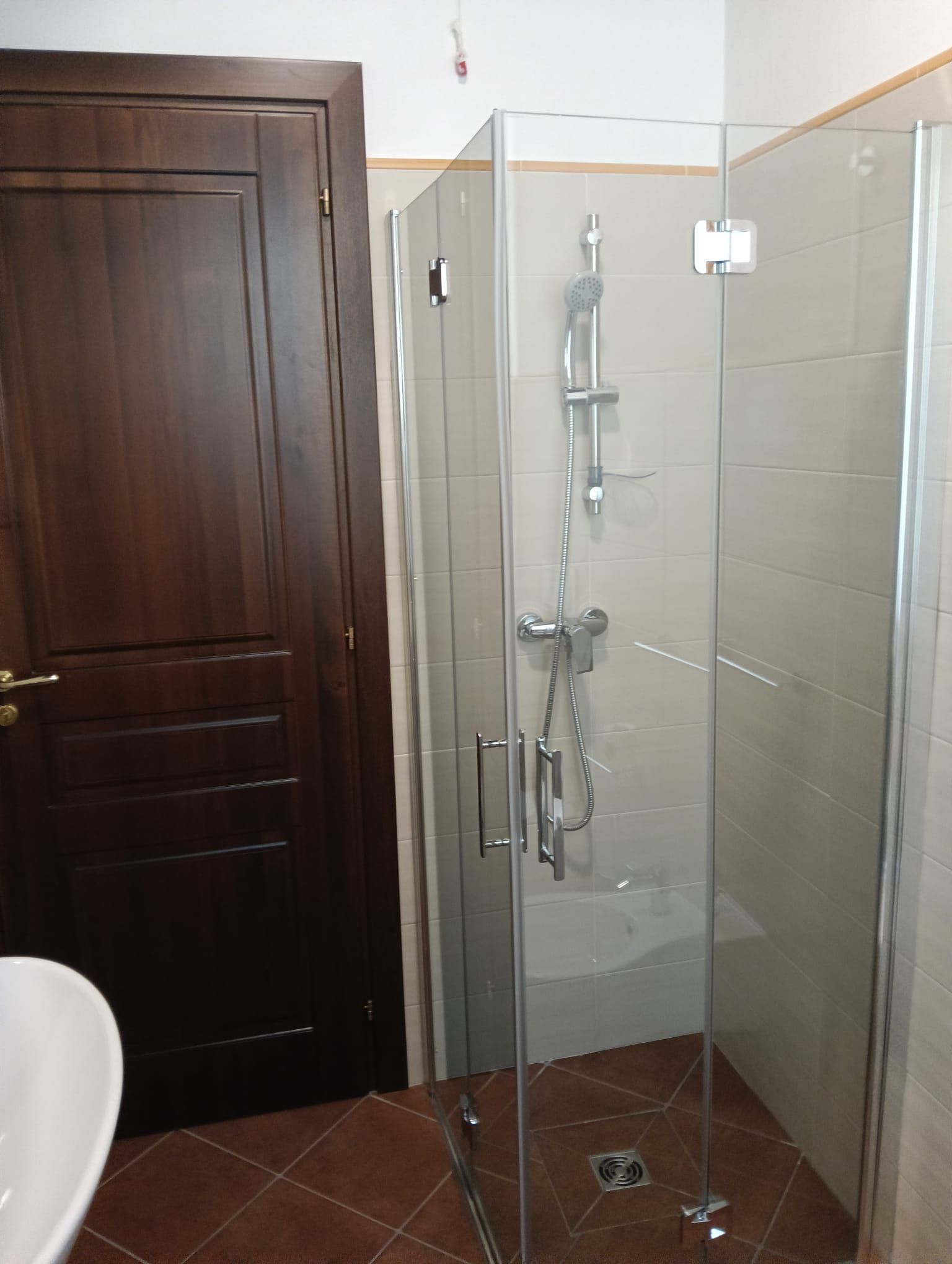 Un piccolo bagno con doccia in vetro, porta marrone e pavimento piastrellato.