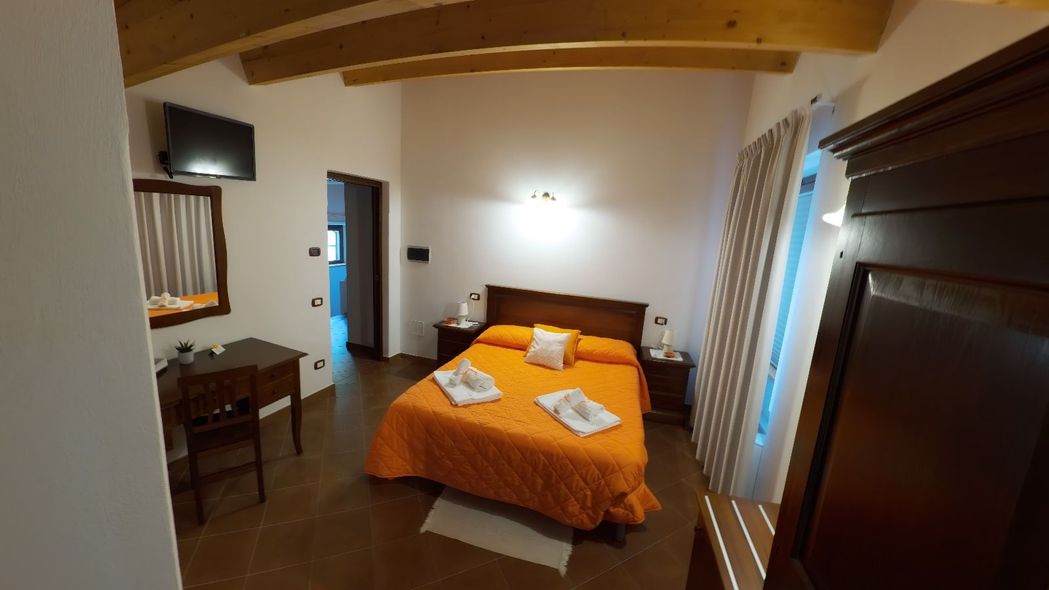 Camera da letto con copriletto arancione, mobili in legno, TV e porta che conduce al bagno.