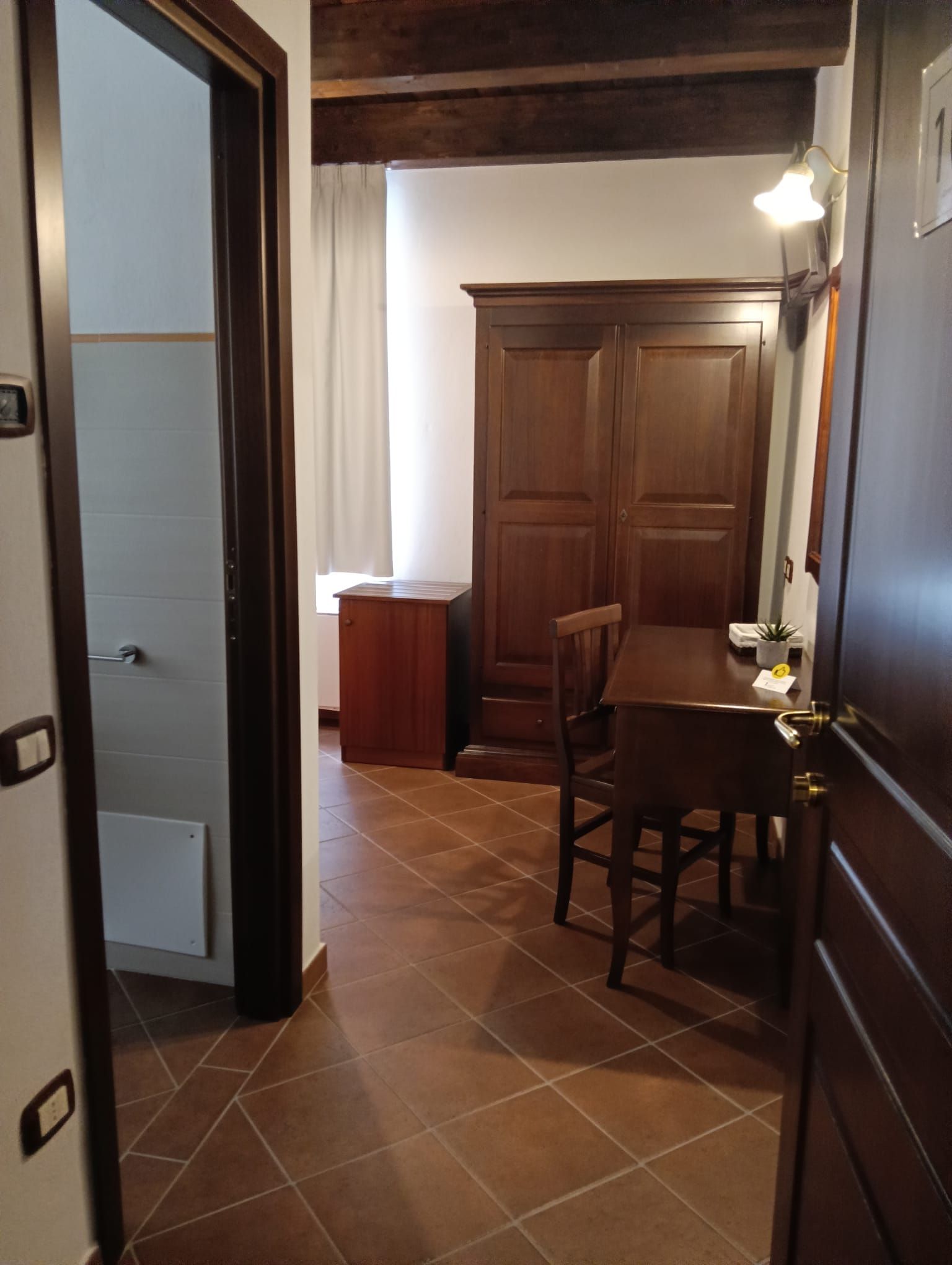 Camera d'albergo interna con mobili in legno scuro, un tavolino e ingresso con bagno.