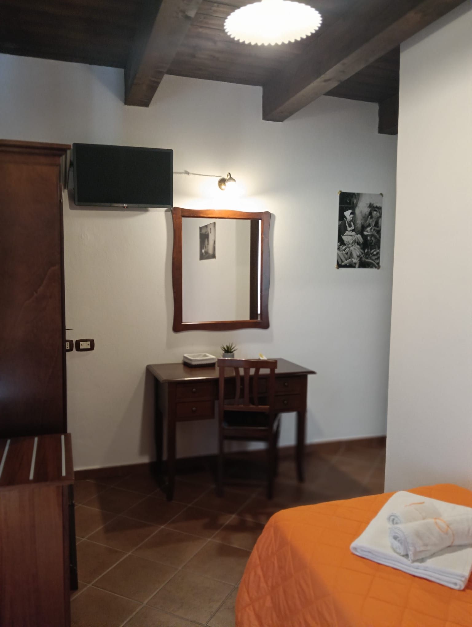 Una camera d'albergo con una scrivania in legno, uno specchio e un letto con una coperta arancione.