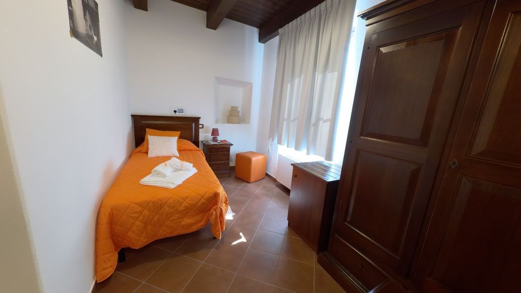 Piccola camera da letto con un letto singolo arancione, armadio in legno scuro e finestra con tende.