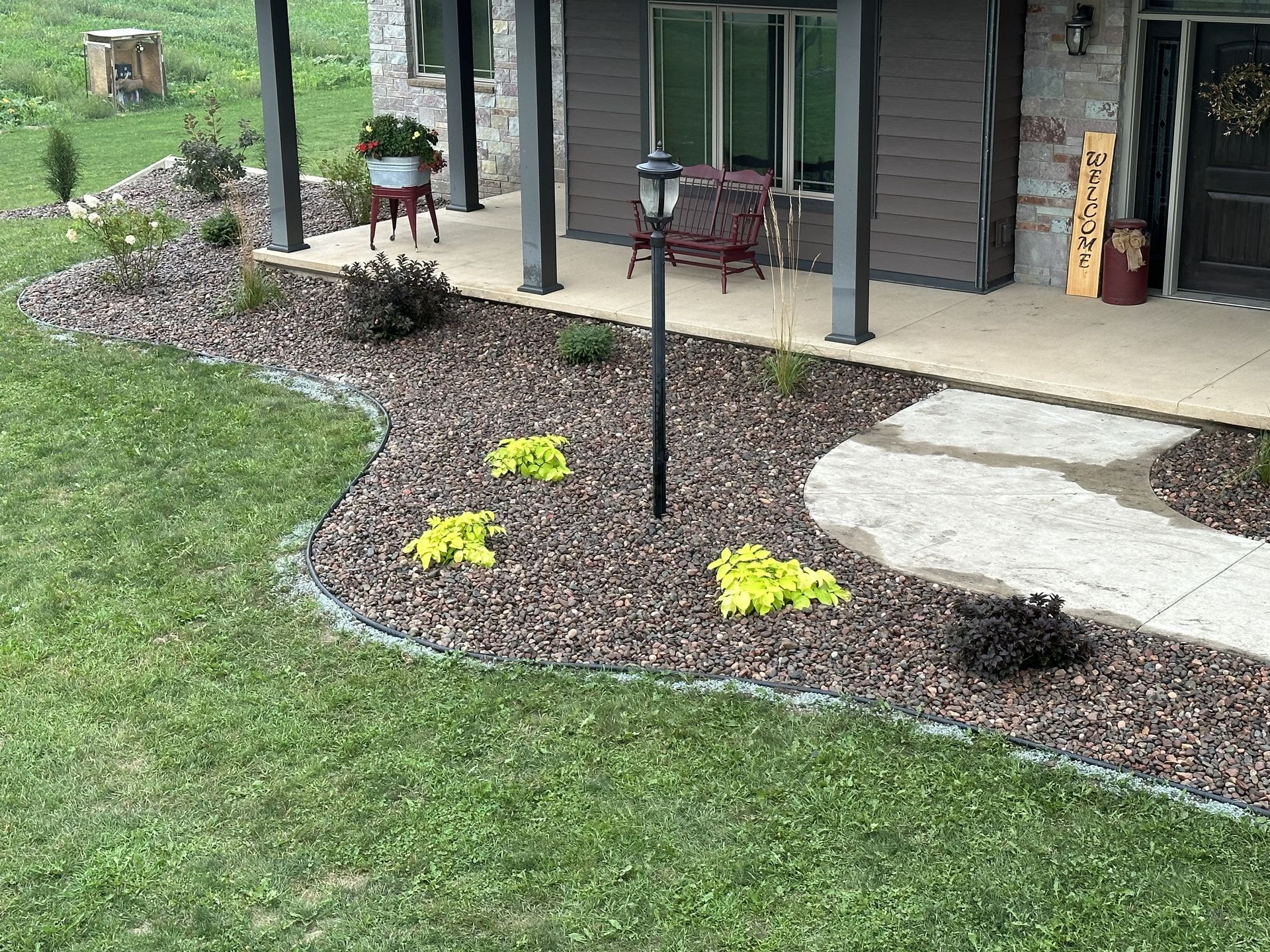 Front yard landscaping with green lawn, mulch beds, yellow flowers, and a covered porch with chairs