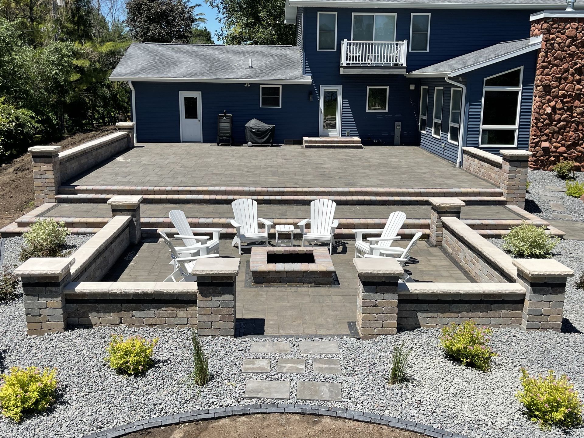 Stone patio with curved steps, central fire pit, and outdoor tables with chairs in a garden courtyard