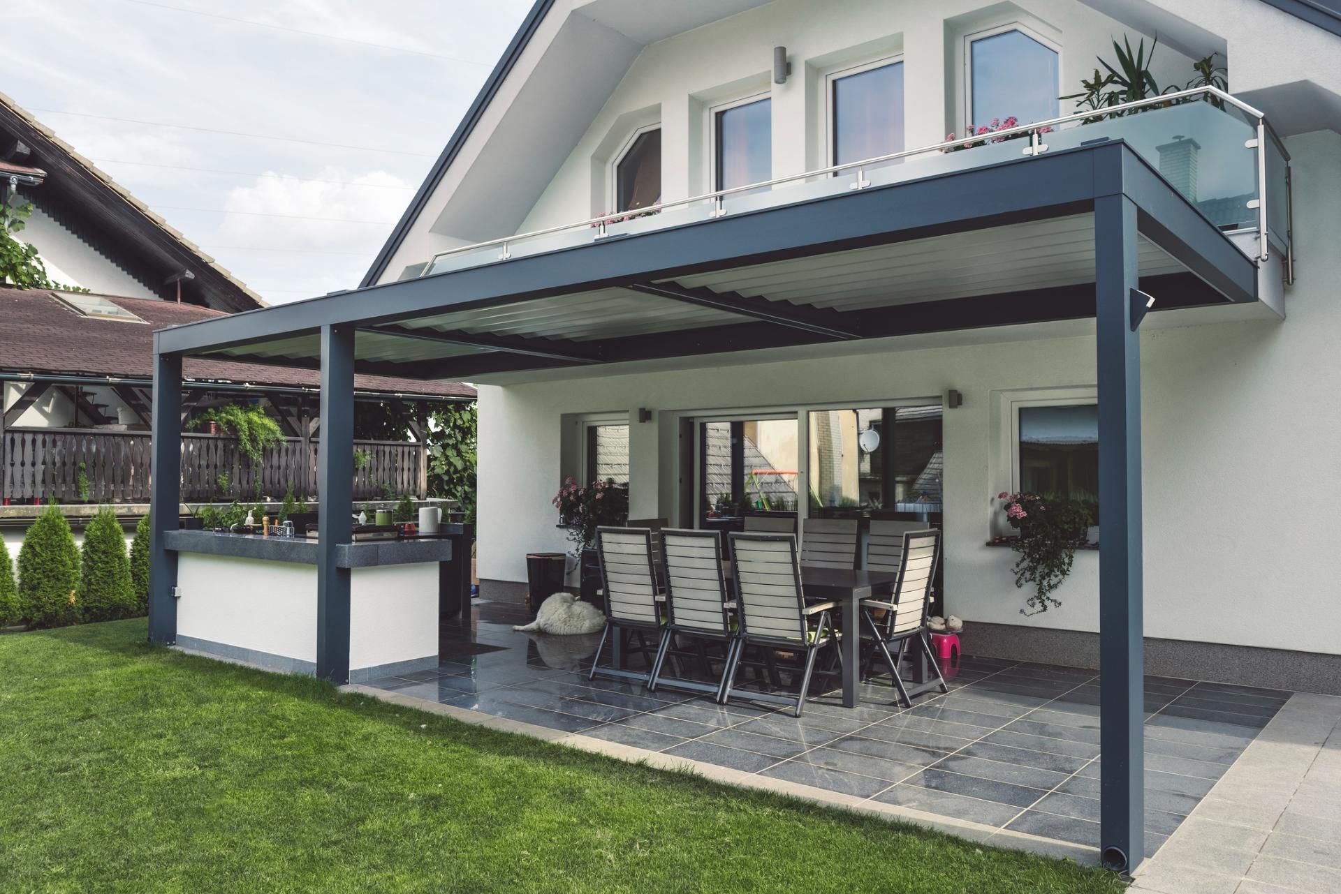 Una casa bianca con un patio con tavolo e sedie sotto un pergolato.