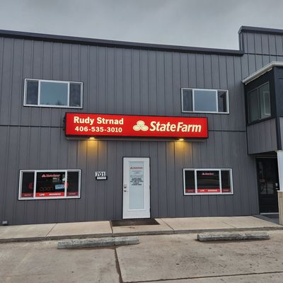 State Farm insurance office exterior with sign, windows, and door. Gray building with red signage.