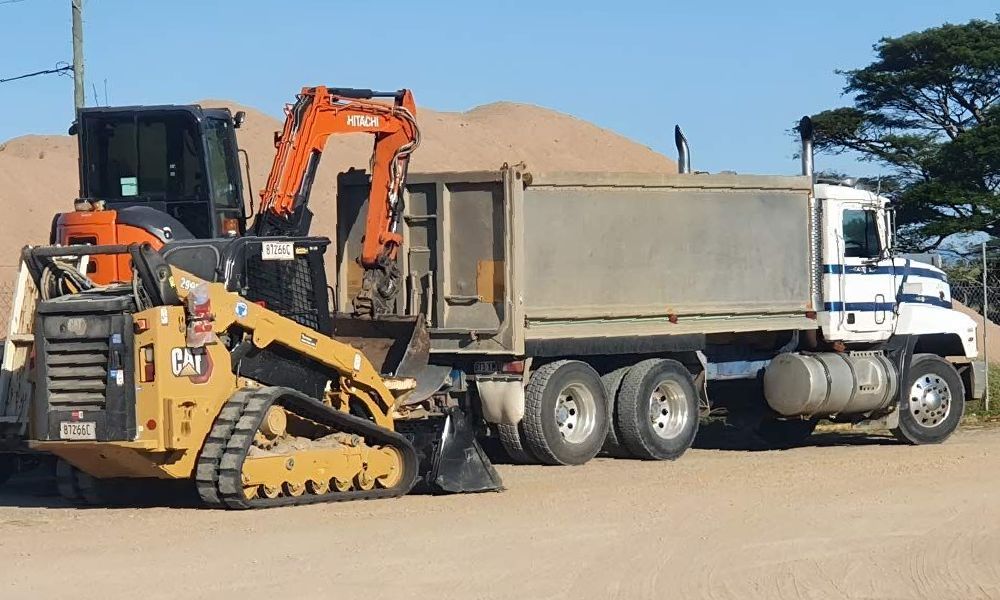 A Bulldozer Is Pulling A Dump Truck On A Dirt Road — Ingham Concrete–Icon in Ingham, QLD