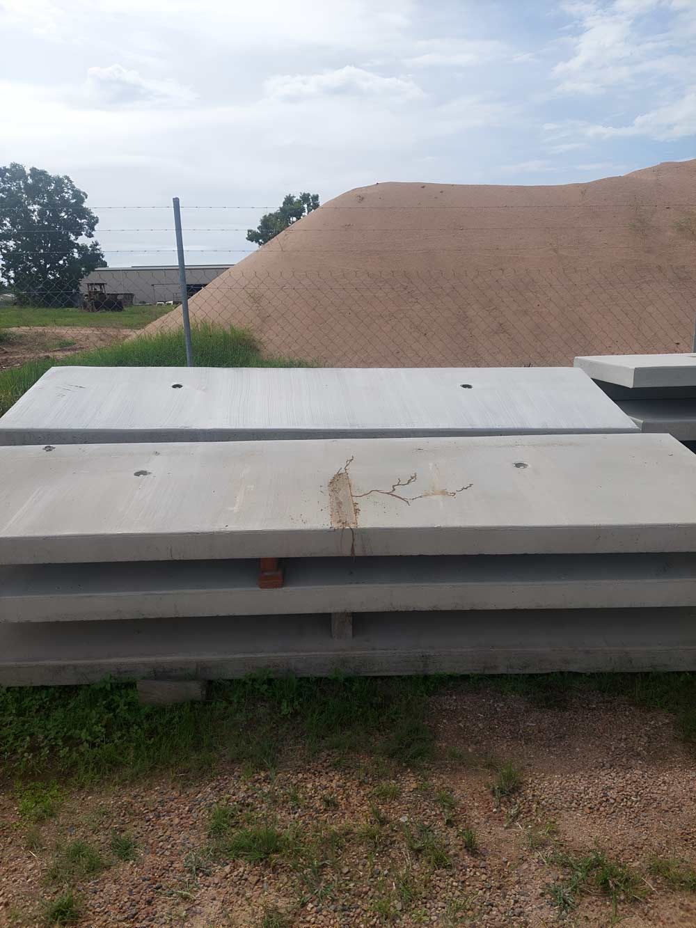 A Pile Of Concrete Slabs Is Sitting In The Grass In Front Of A Pile Of Sand — Ingham Concrete–Icon in Ingham, QLD