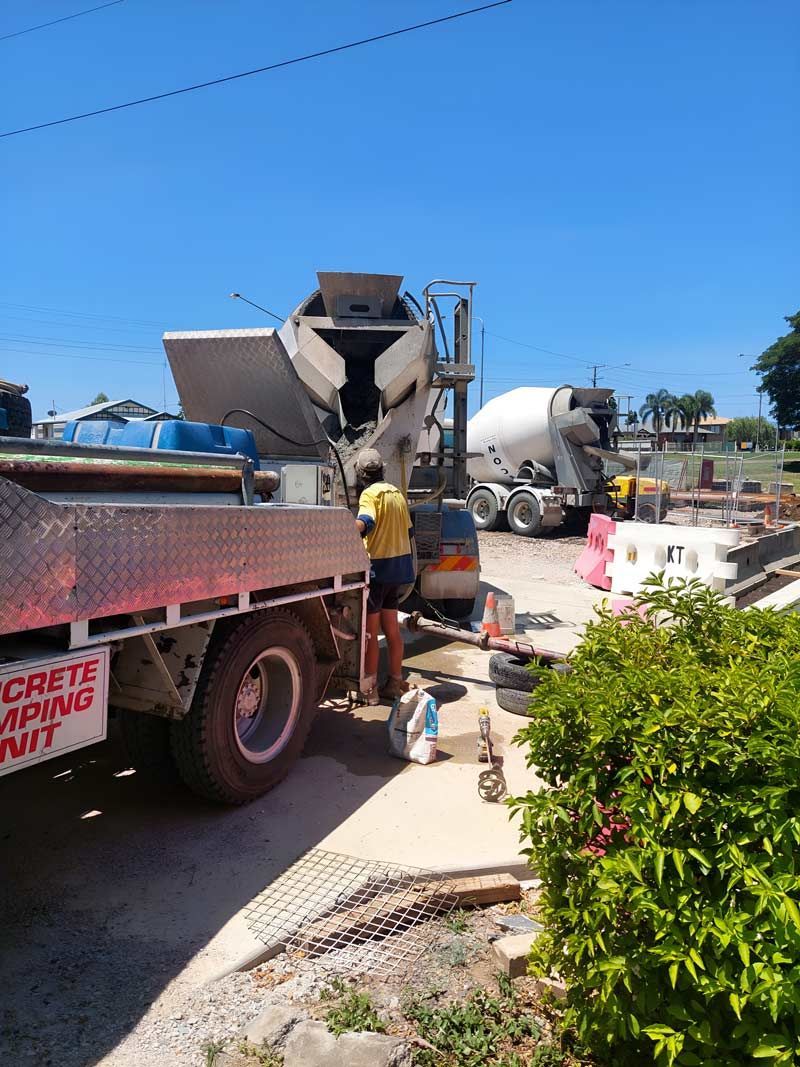 A Man Is Standing Next To A Concrete Mixer Truck — Ingham Concrete–Icon in Ingham, QLD
