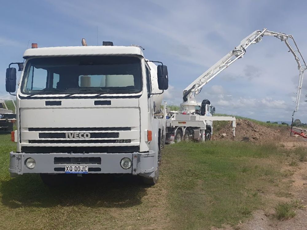 A White Iveco Concrete Mixer  Truck Is Parked In A Grassy Field — Ingham Concrete–Icon in Ingham, QLD