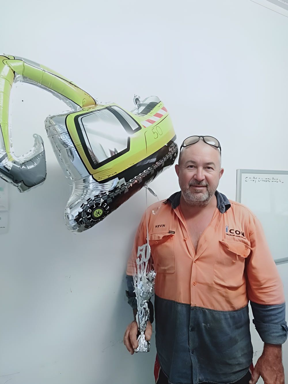 Man In An Orange Shirt Is Standing In With Balloon Excavator — Ingham Concrete–Icon in Ingham, QLD